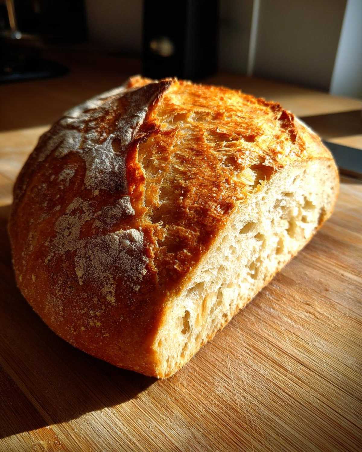 Świeżo upieczony bochenek chleba z chrupiącą skórką, posypany mąką, leżący na drewnianej desce. mąką pełnoziarnista lubella przepis na chleb.