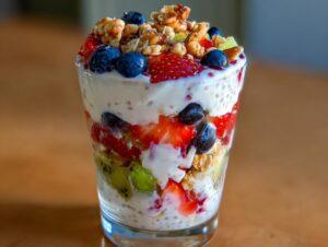 Zbliżenie na warstwowy deser z chia z jogurtem, truskawkami, borówkami, kiwi i orzechami w szklance.