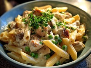 Zbliżenie miski makaronu penne z kremowym sosem, kawałkami kurczaka, zielonym groszkiem i świeżą natką pietruszki. makaron z serkiem philadelphia.