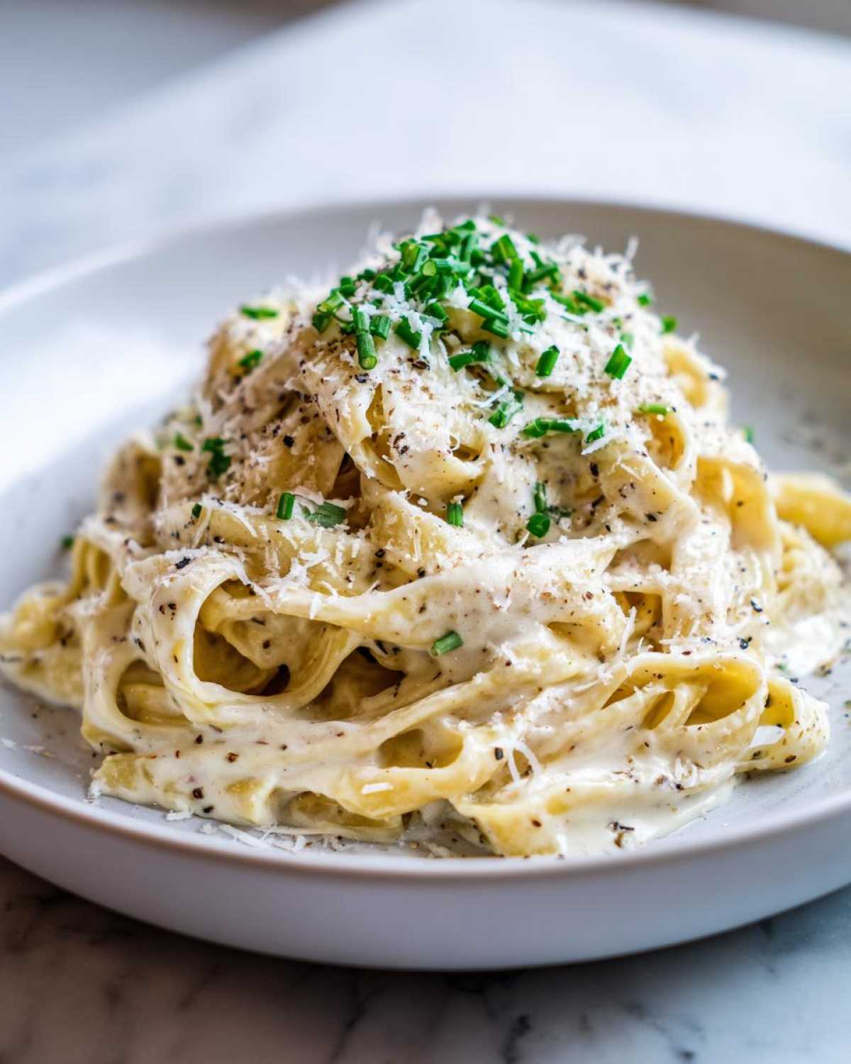 Zbliżenie na makaron z sosem śmietanowo truflowym, posypany szczypiorkiem i parmezanem.