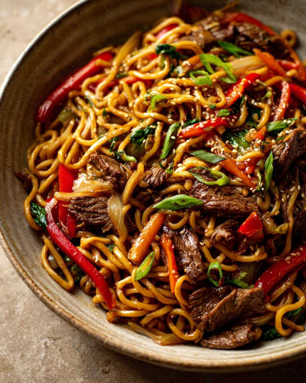 Zbliżenie miski z daniem makaron udon z wolowina, papryką, cebulą i zieloną cebulką, posypane sezamem.