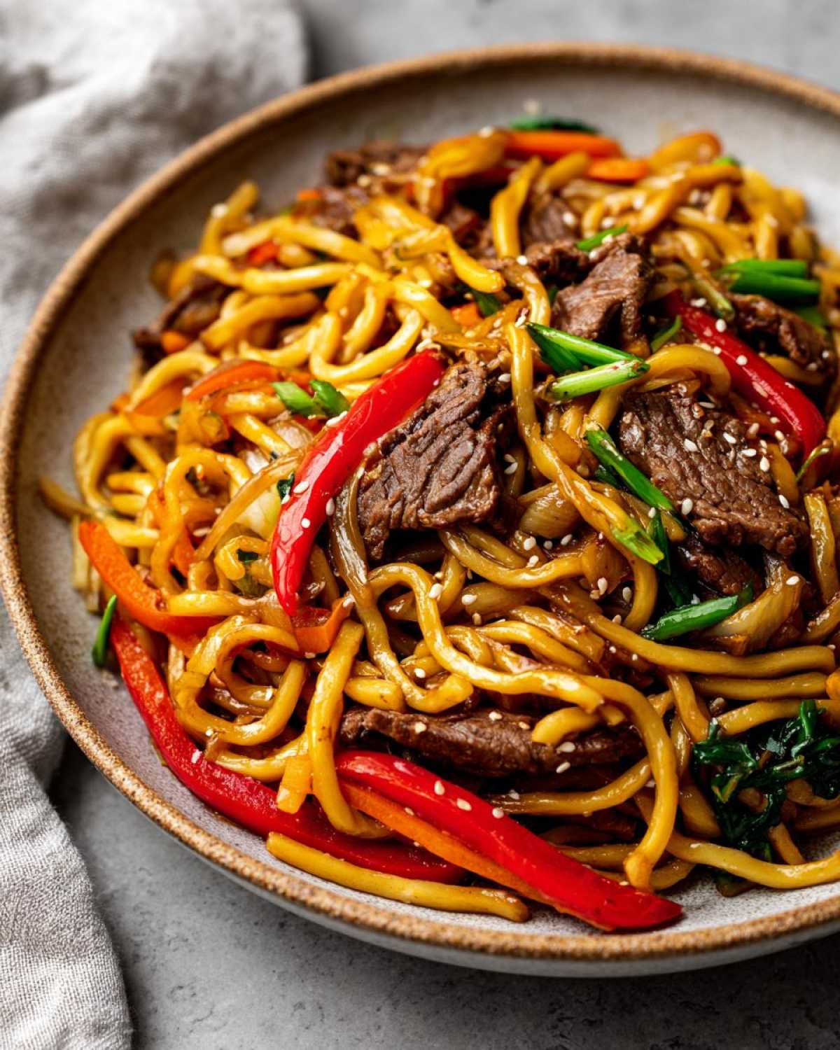 Zbliżenie miski z makaronem udon z wołowiną, papryką, cebulą i sezamem.