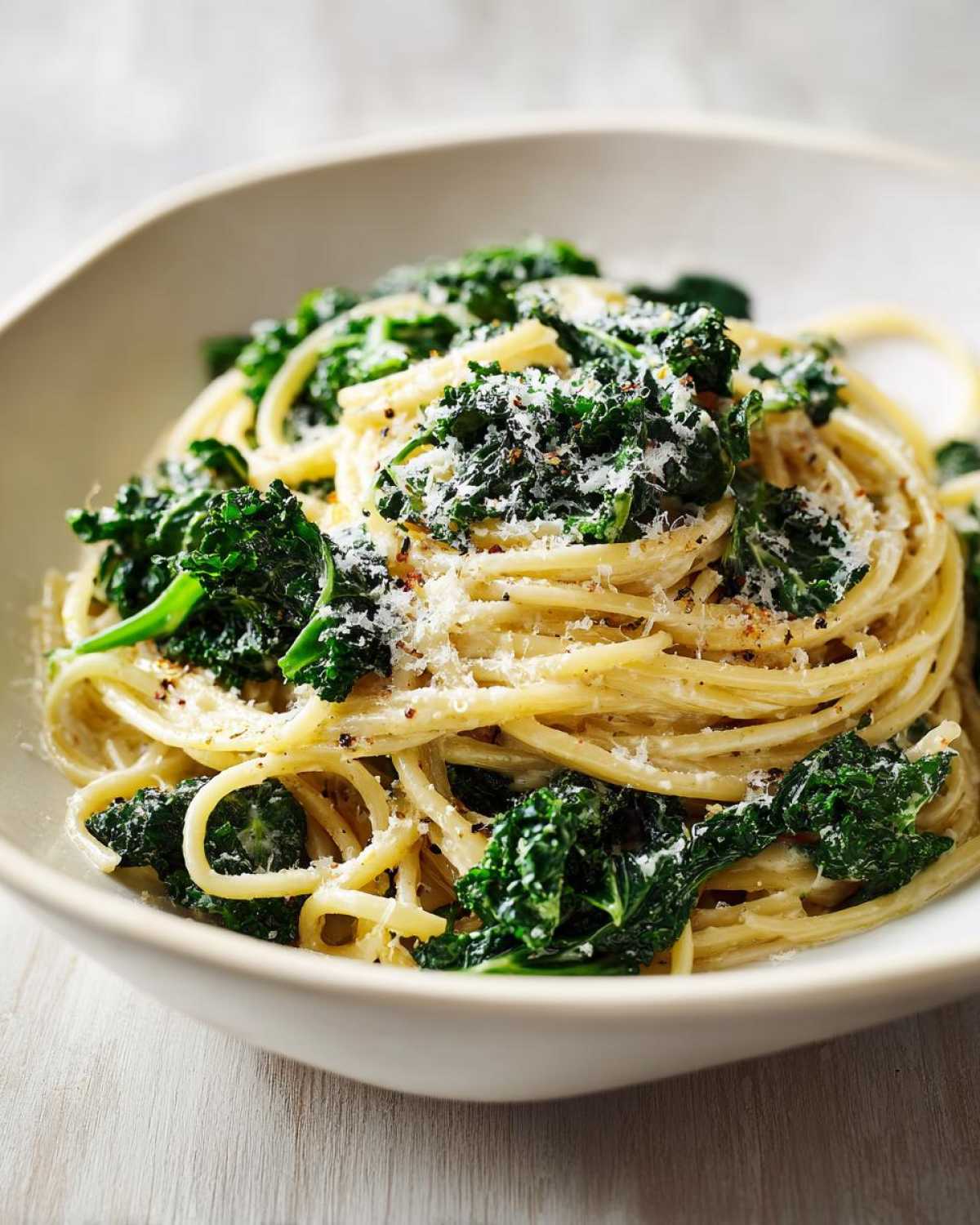 Zbliżenie miski makaronu spaghetti z jarmużem, posypanego parmezanem i pieprzem, w kremowym sosie. makaron z jarmużem w sosie śmietanowym.