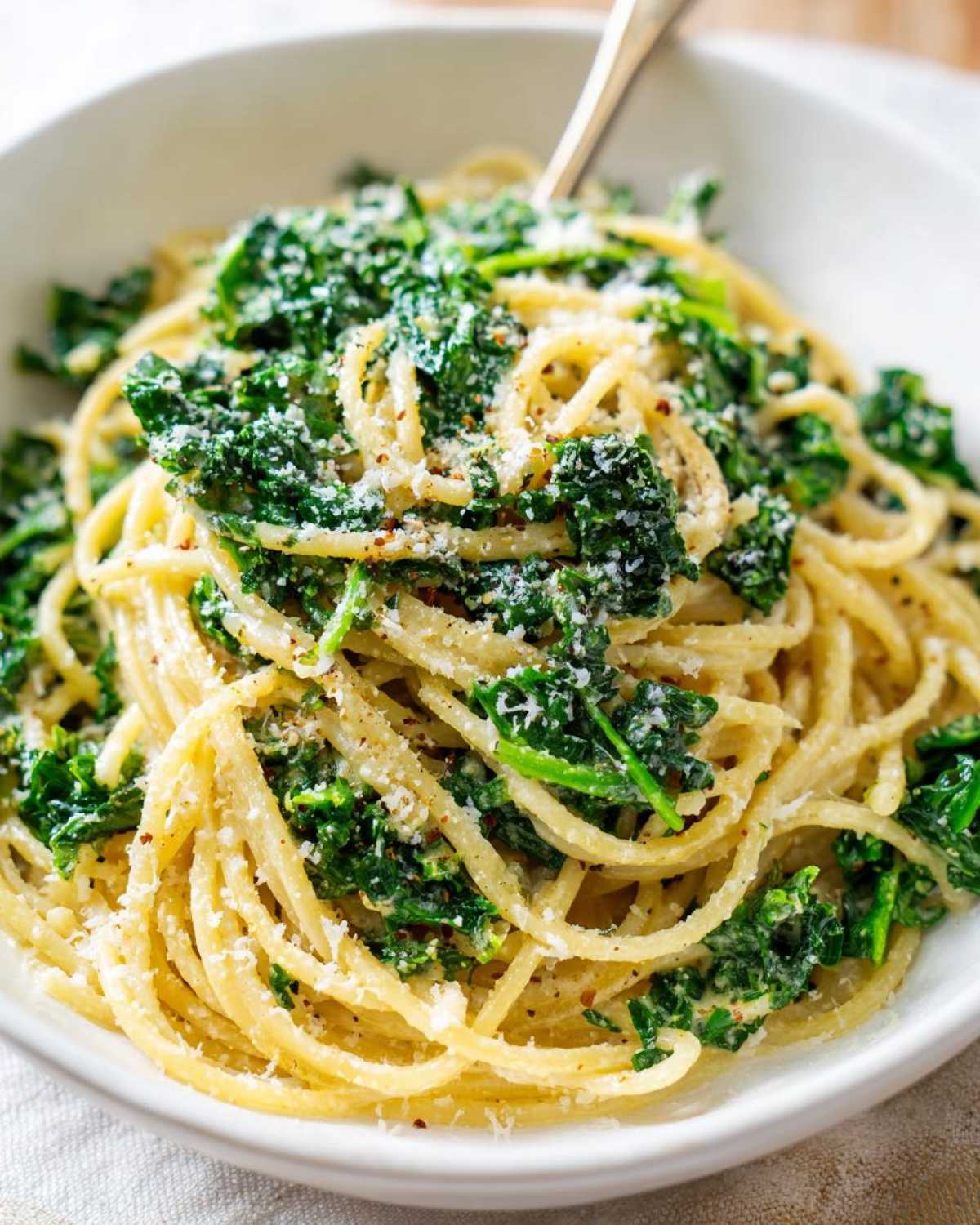 Zbliżenie miski z makaronem spaghetti z jarmużem w sosie śmietanowym, posypanym parmezanem i pieprzem.