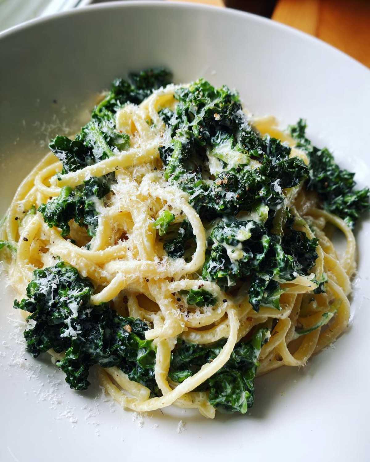 Zbliżenie na makaron z jarmużem w sosie śmietanowym, posypany startym parmezanem i świeżo zmielonym pieprzem.