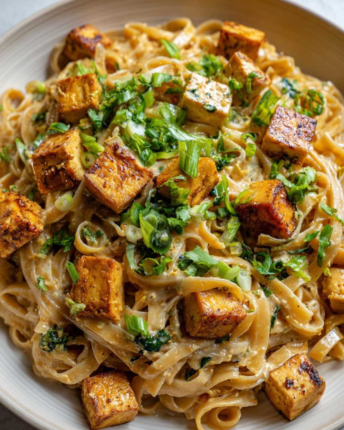Zbliżenie miski z makaronem z tofu i mlekiem kokosowym, posypanym zieloną cebulką.