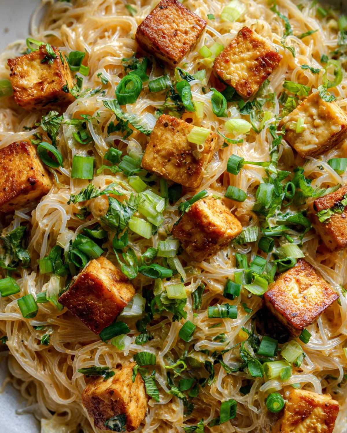 Zbliżenie na makaron z tofu i mlekiem kokosowym, posypany świeżym szczypiorkiem i ziołami.