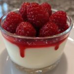 Zbliżenie na szklankę panna cotta oryginalny przepis z sosem malinowym i świeżymi malinami na wierzchu.