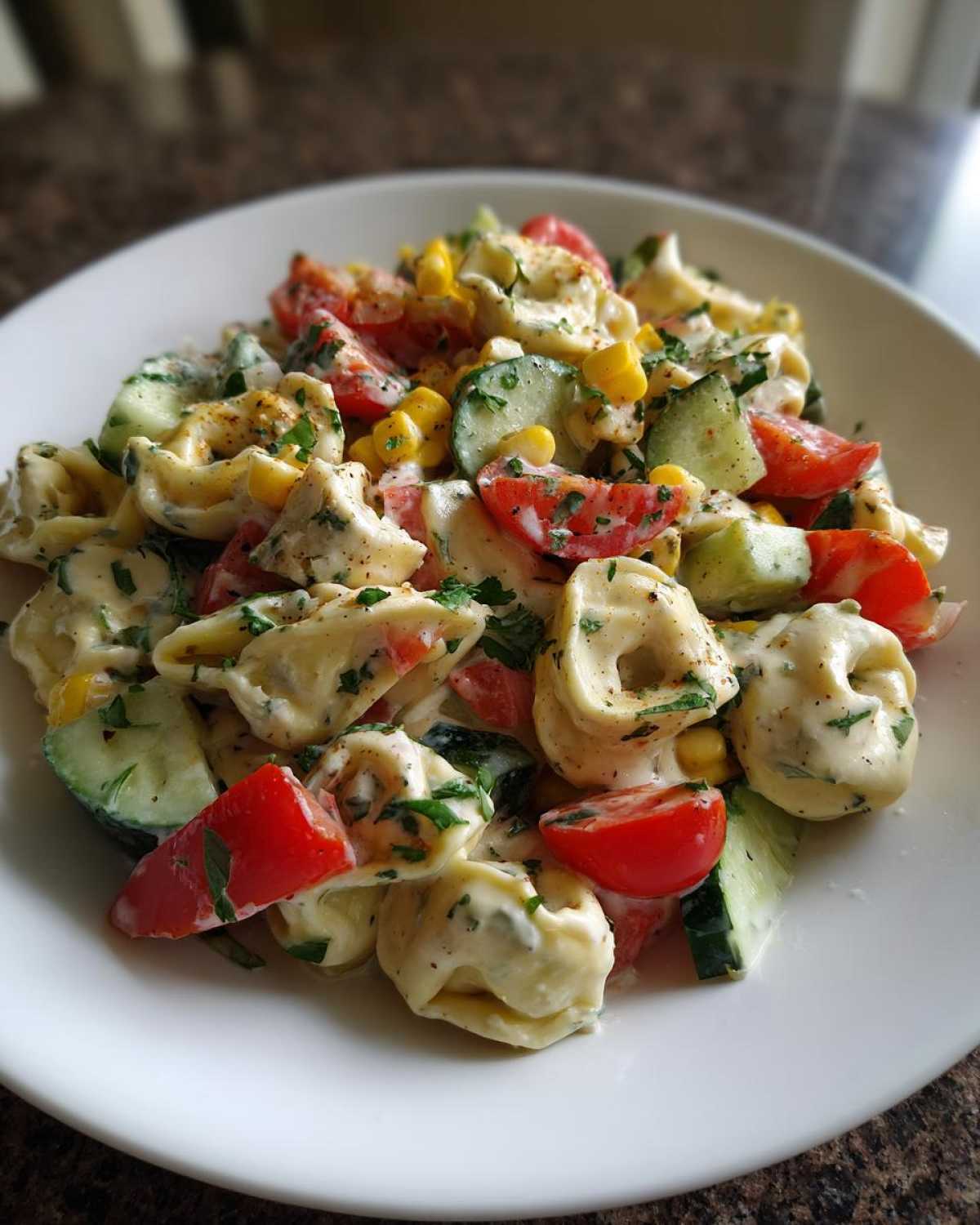 Zbliżenie na sałatkę z tortellini, pomidorami, ogórkiem, kukurydzą i sosem, posypaną natką pietruszki. sałatka z tortellini
