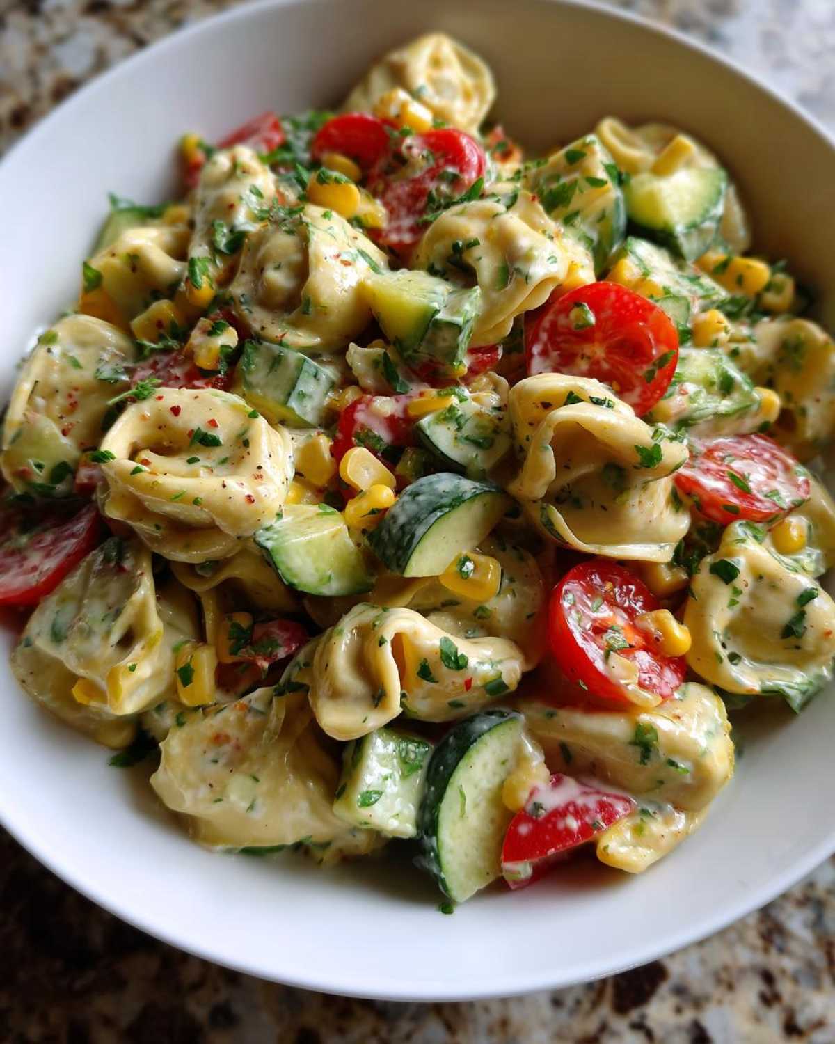 Zbliżenie na sałatka z tortellini z pomidorami, ogórkiem i kukurydzą, posypana ziołami.
