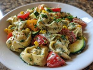 Zbliżenie na sałatkę z tortellini z pomidorami, cukinią, kukurydzą i sosem, posypaną świeżymi ziołami.