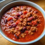 Zdjęcie z bliska miski z chili con carne, z widocznymi kawałkami mięsa, fasoli i pomidorów.