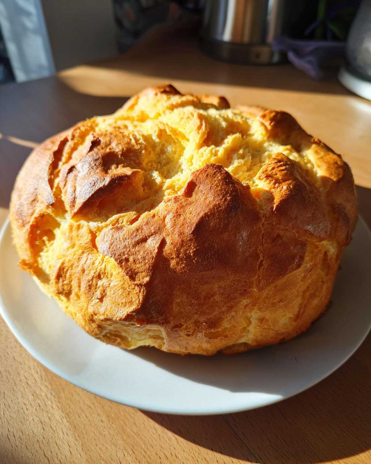 Zdjęcie przedstawia cały, upieczony chleb chmurowy na białym talerzu, o złocistej barwie.