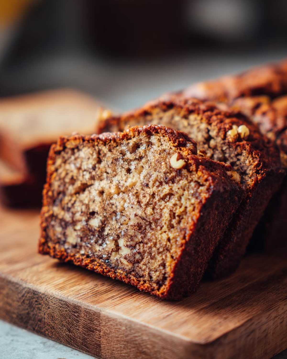Kawałki chlebek bananowy ułożone na drewnianej desce. Widoczne orzechy i wilgotna struktura.