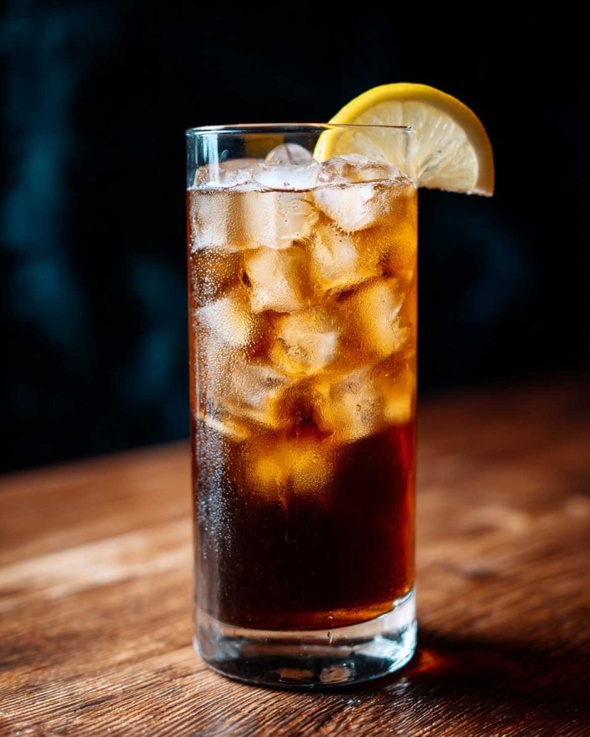 Szklanka espresso tonic z lodem i plasterkiem cytryny na drewnianym blacie.
