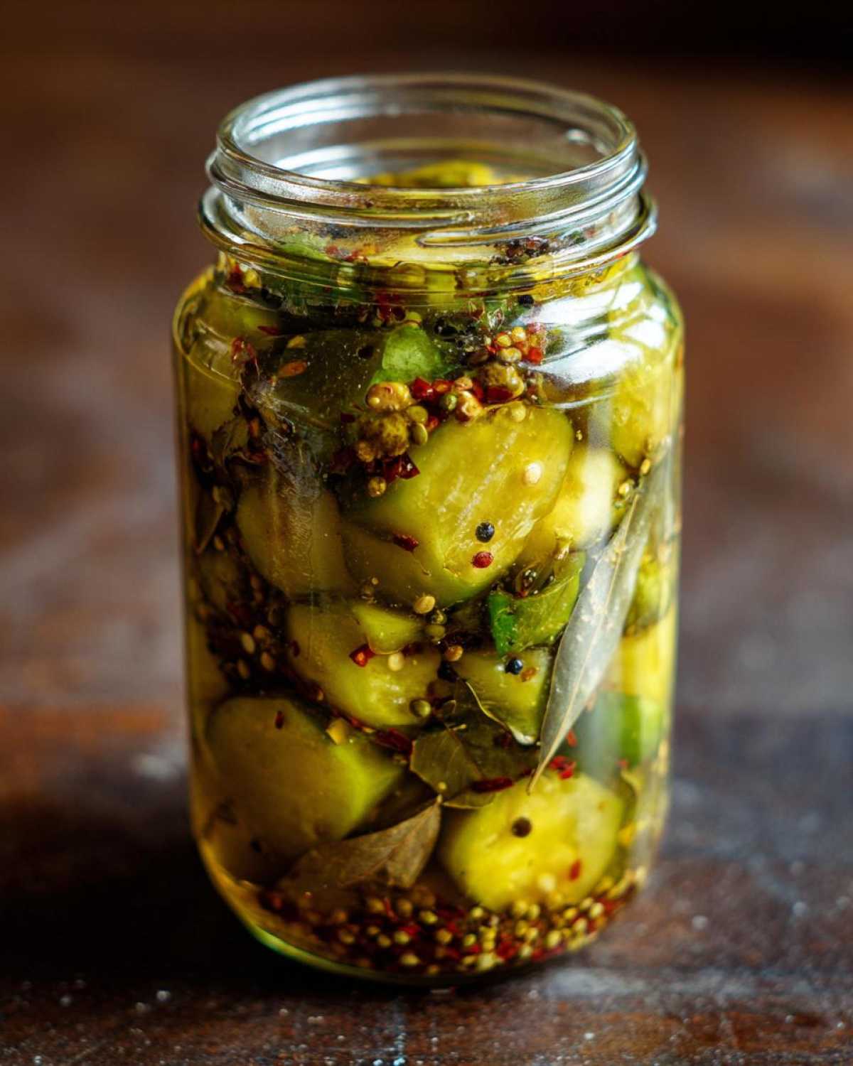 Słoik z kawałkami kiszonego mango, liśćmi laurowymi i ziarnami pieprzu.