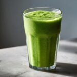 Szklanka pełna zielonego koktajlu szpinakowo-bananowego na jasnym tle. Idealny napój na szybkie śniadanie.