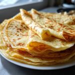 Stos apetycznych naleśników budyniowych na białym talerzu, zwinięte w ruloniki.