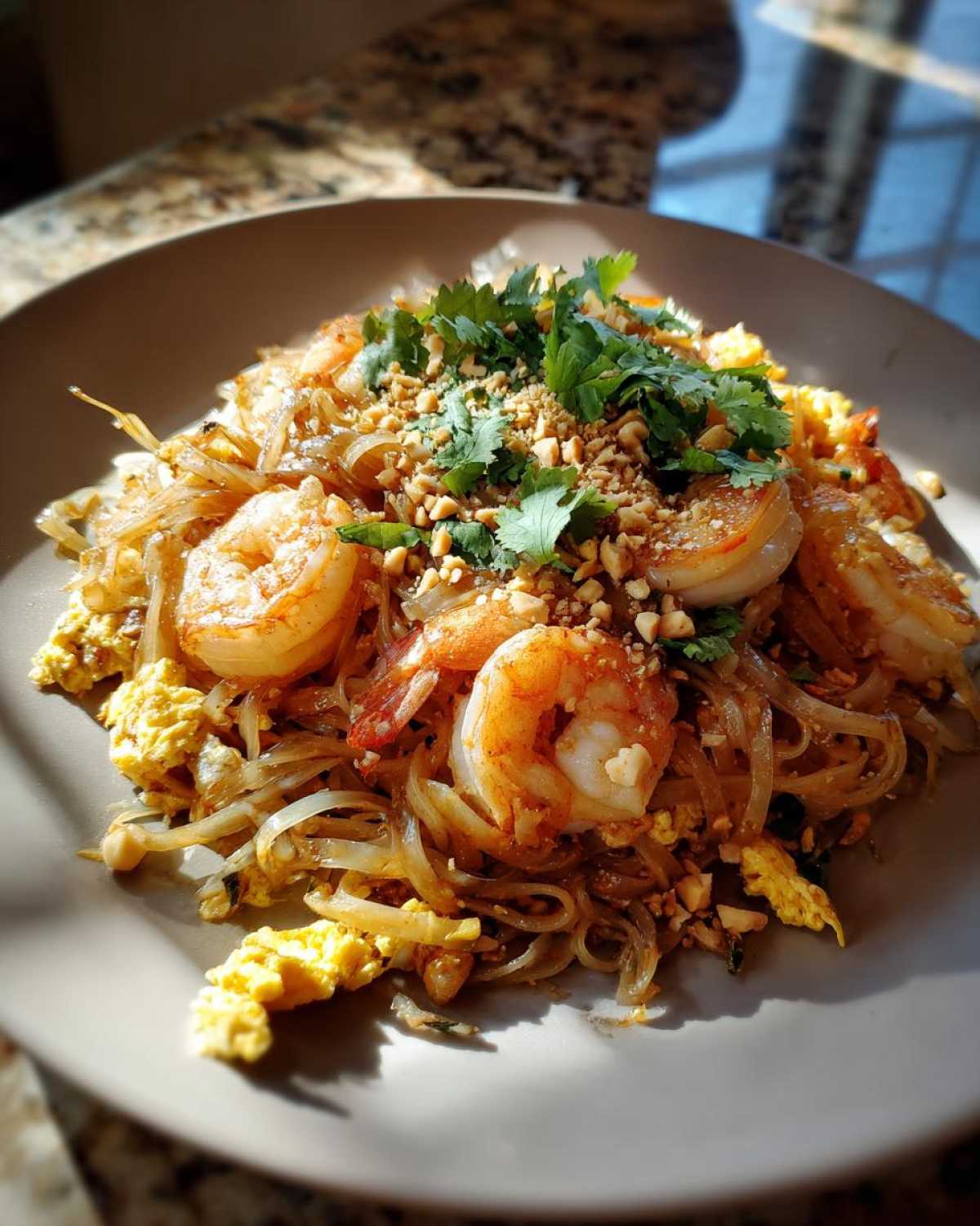 Apetyczne danie Pad Thai z krewetkami, orzechami i kolendrą na talerzu.