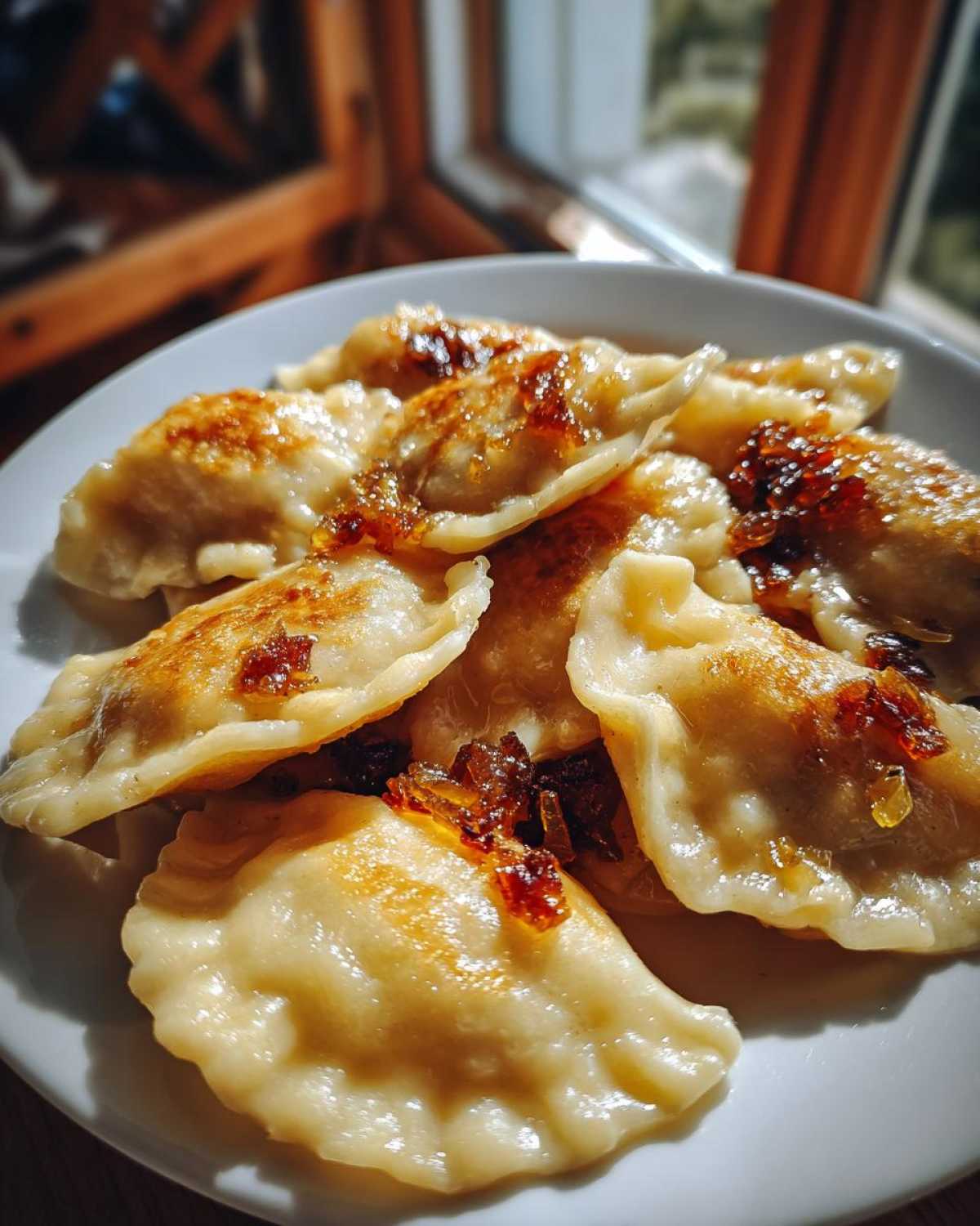 Zbliżenie na talerz pełen pierogów ruskich tradycyjnych, polanych skarmelizowaną cebulką.