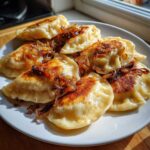 Talerz pełen pierogów ruskich tradycyjnych, polanych podsmażoną cebulką.