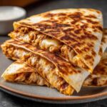 Zdjęcie quesadilla z kurczakiem, z serem i kurczakiem, ułożonej na talerzu.