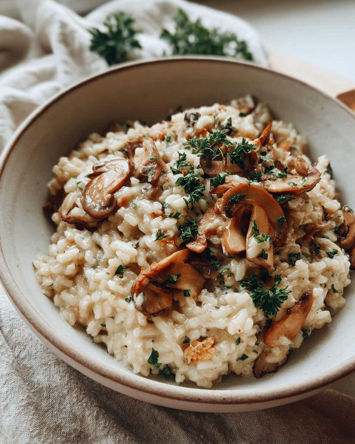 Kremowe risotto z grzybami leśnymi, udekorowane świeżą natką pietruszki.