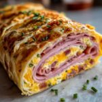 Przekrój rollsa z tortilli z szynką, jajecznicą i serem, posypany szczypiorkiem.
