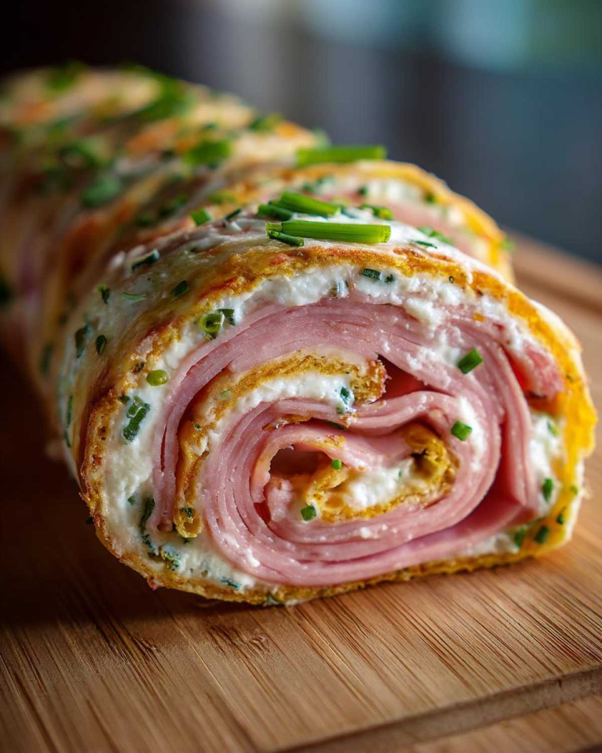 Zdjęcie z bliska rollsy z tortilli z szynką, kremowym serem i szczypiorkiem na drewnianej desce.