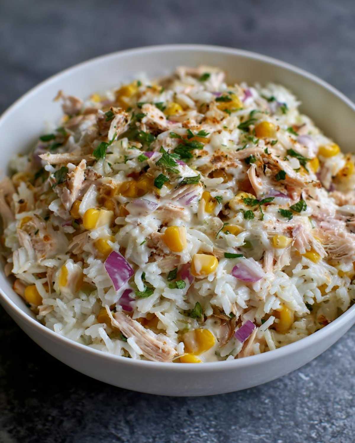 Zdjęcie z bliska sałatki z tuńczykiem i ryżem w białej misce, z kukurydzą, czerwoną cebulą i ziołami.