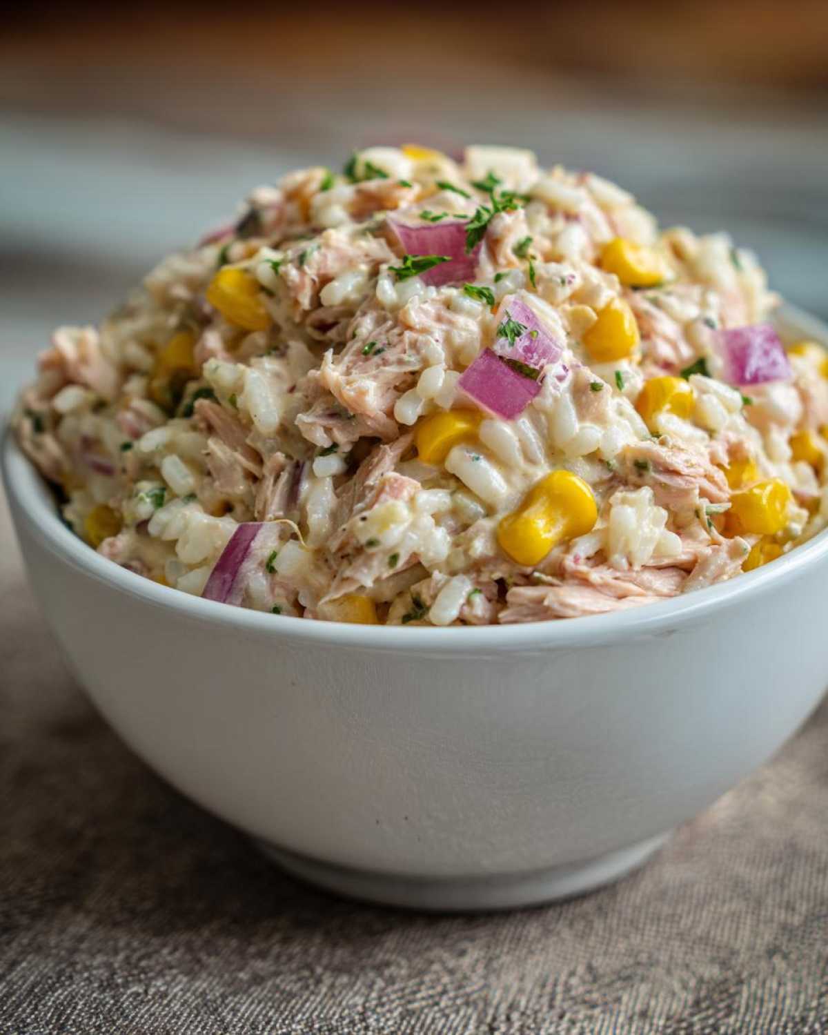 Biała miska pełna sałatki z tuńczykiem i ryżem, z kukurydzą i czerwoną cebulą.