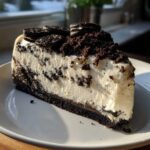 Kawałek sernika Oreo bez pieczenia na talerzu, ozdobiony ciasteczkami Oreo i pokruszonymi ciasteczkami.