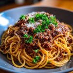 Apetyczne spaghetti bolognese na talerzu, posypane parmezanem i świeżą pietruszką. Klasyczne danie włoskie.