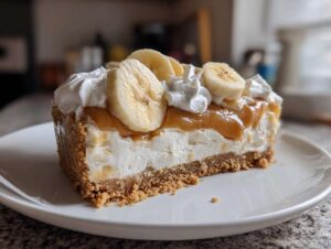 Kawałek pysznego banoffee pie bez pieczenia z kremem, bananami i karmelem na białym talerzu.