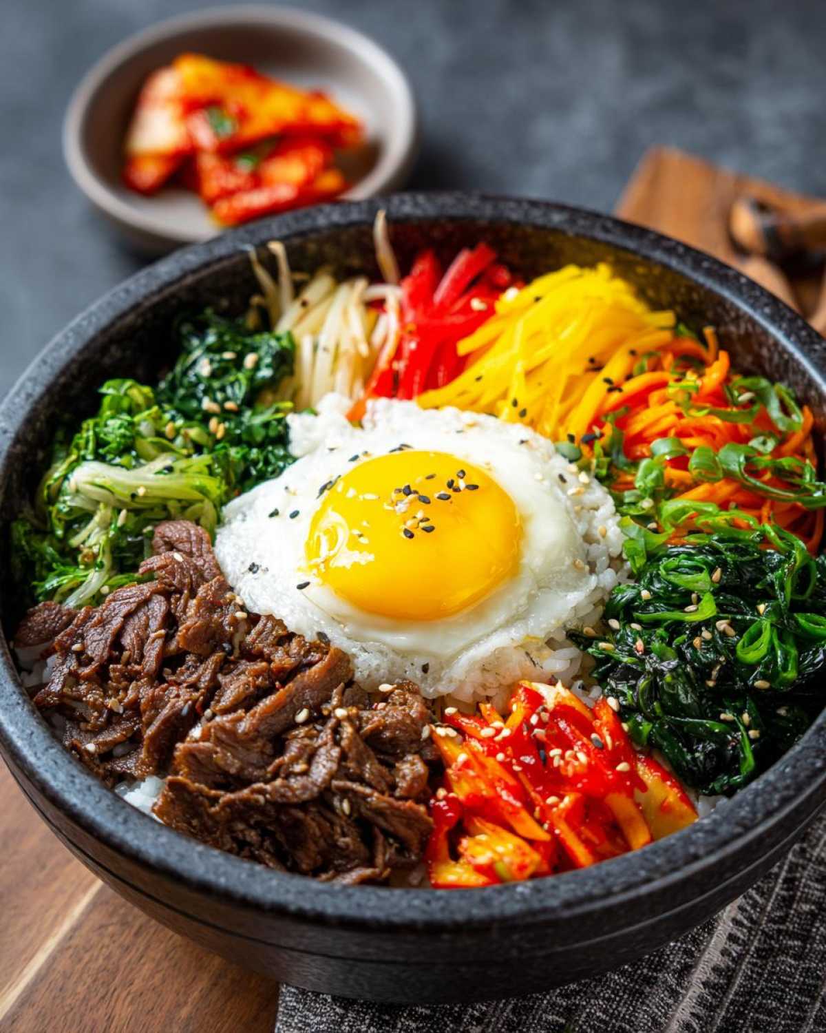 Zbliżenie na miskę bibimbap z ryżem, wołowiną, jajkiem sadzonym i kolorowymi warzywami.