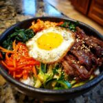 Zbliżenie na miskę bibimbap z ryżem, wołowiną, marchewką, szpinakiem, kimchi i sadzonym jajkiem na wierzchu.