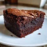 Kawałek wilgotnego brownie z whisky na białym talerzyku, z widoczną chrupiącą skórką.