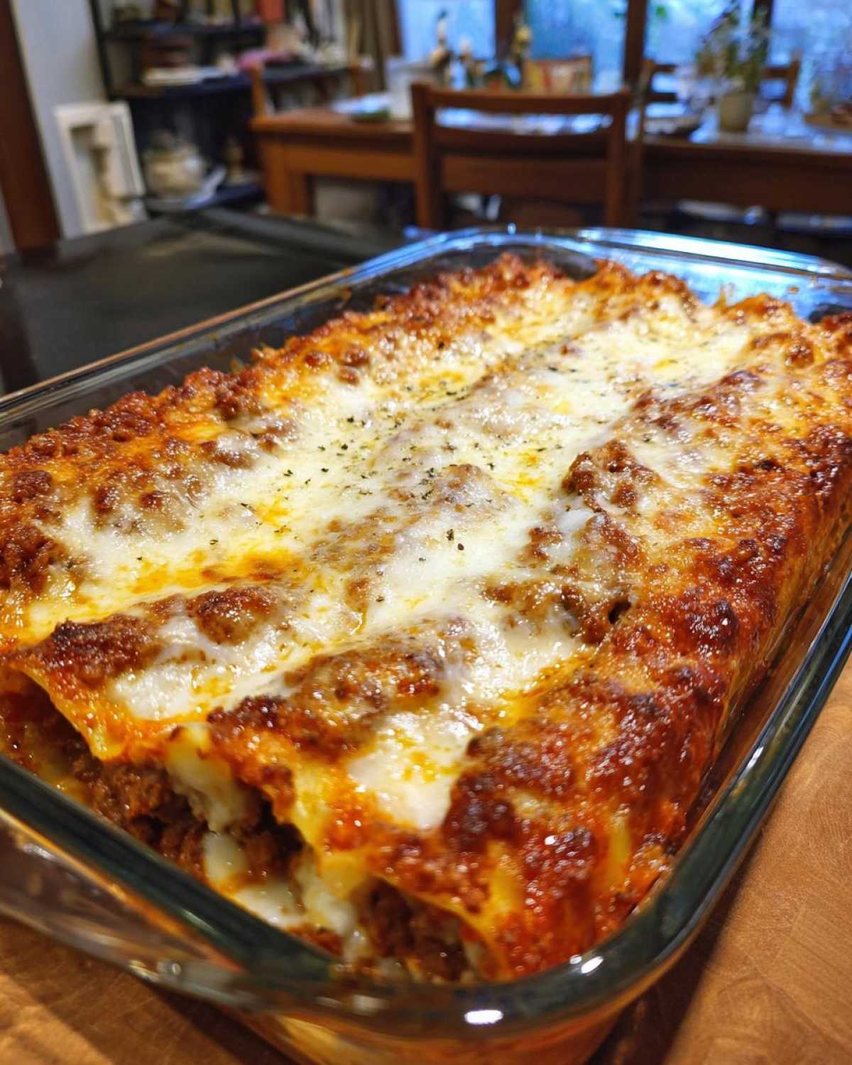 Zbliżenie na zapiekane Cannelloni z mięsem, pokryte ciągnącym się serem i ziołami, w szklanym naczyniu.