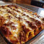 Zbliżenie na zapiekane Cannelloni z mięsem, polane sosem pomidorowym i posypane ciągnącym się serem.