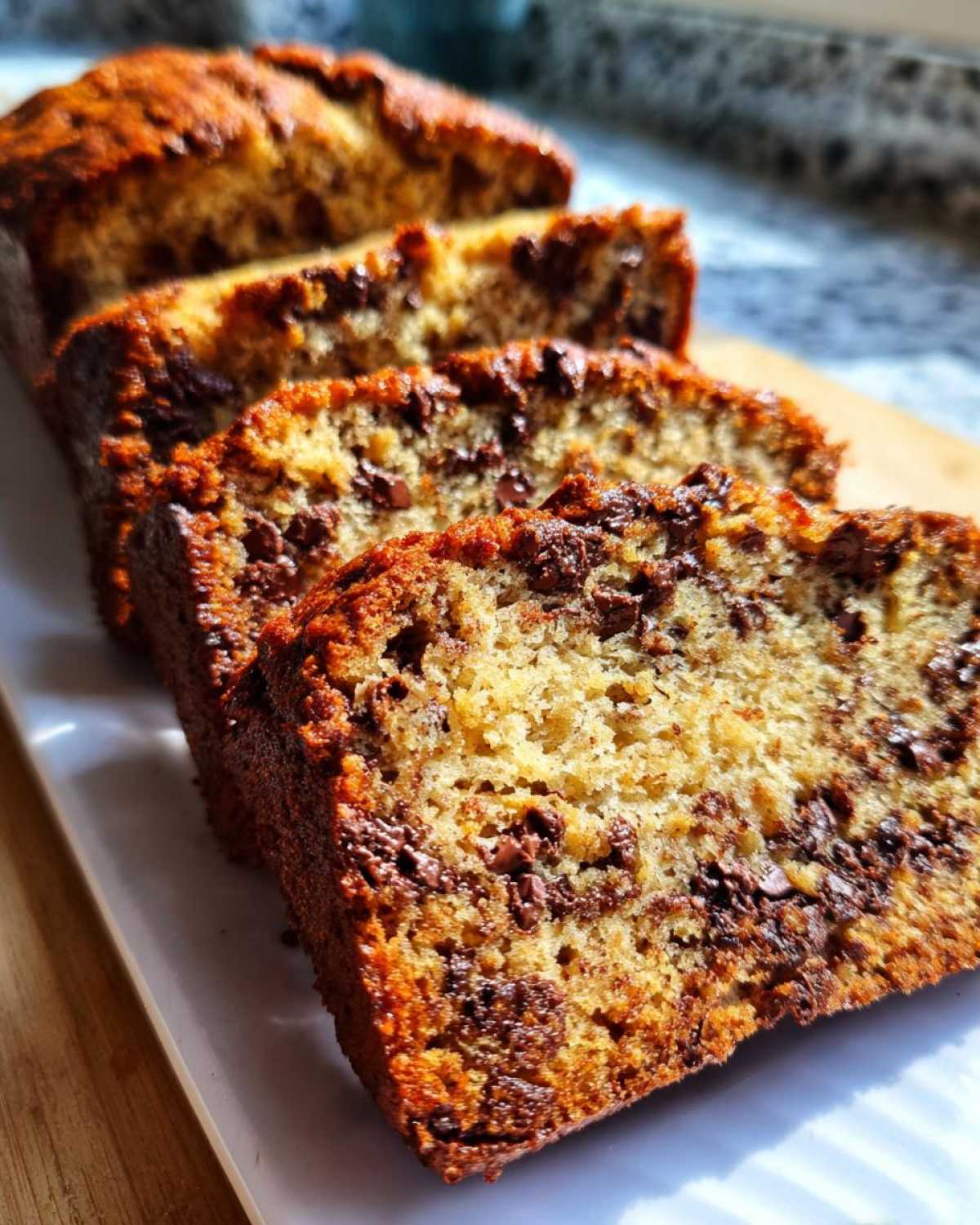 Pokrojony chleb bananowy z kawałkami czekolady na białym talerzu.
