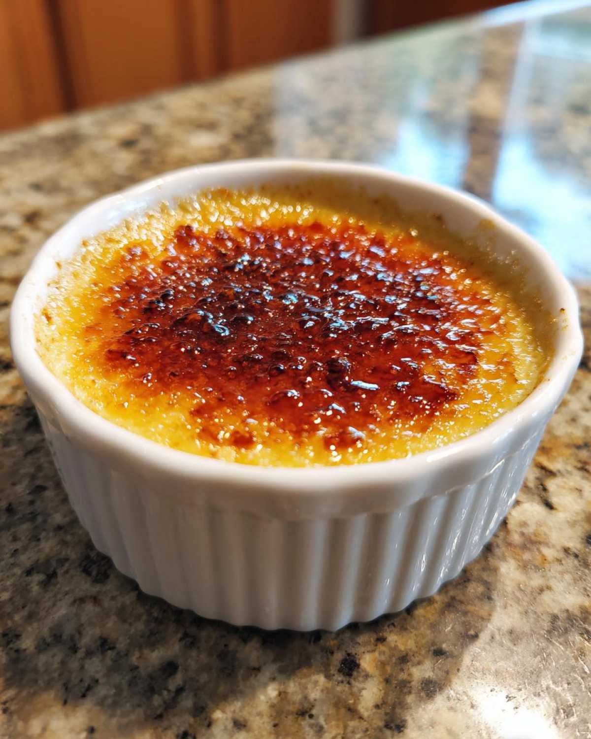 Zbliżenie na idealnie przygotowane Crème brûlée w białej kokilce z chrupiącą, karmelizowaną skorupką.