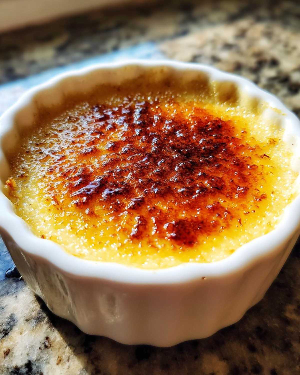 Zbliżenie na kremową Crème brûlée z chrupiącą, karmelizowaną warstwą cukru na wierzchu.