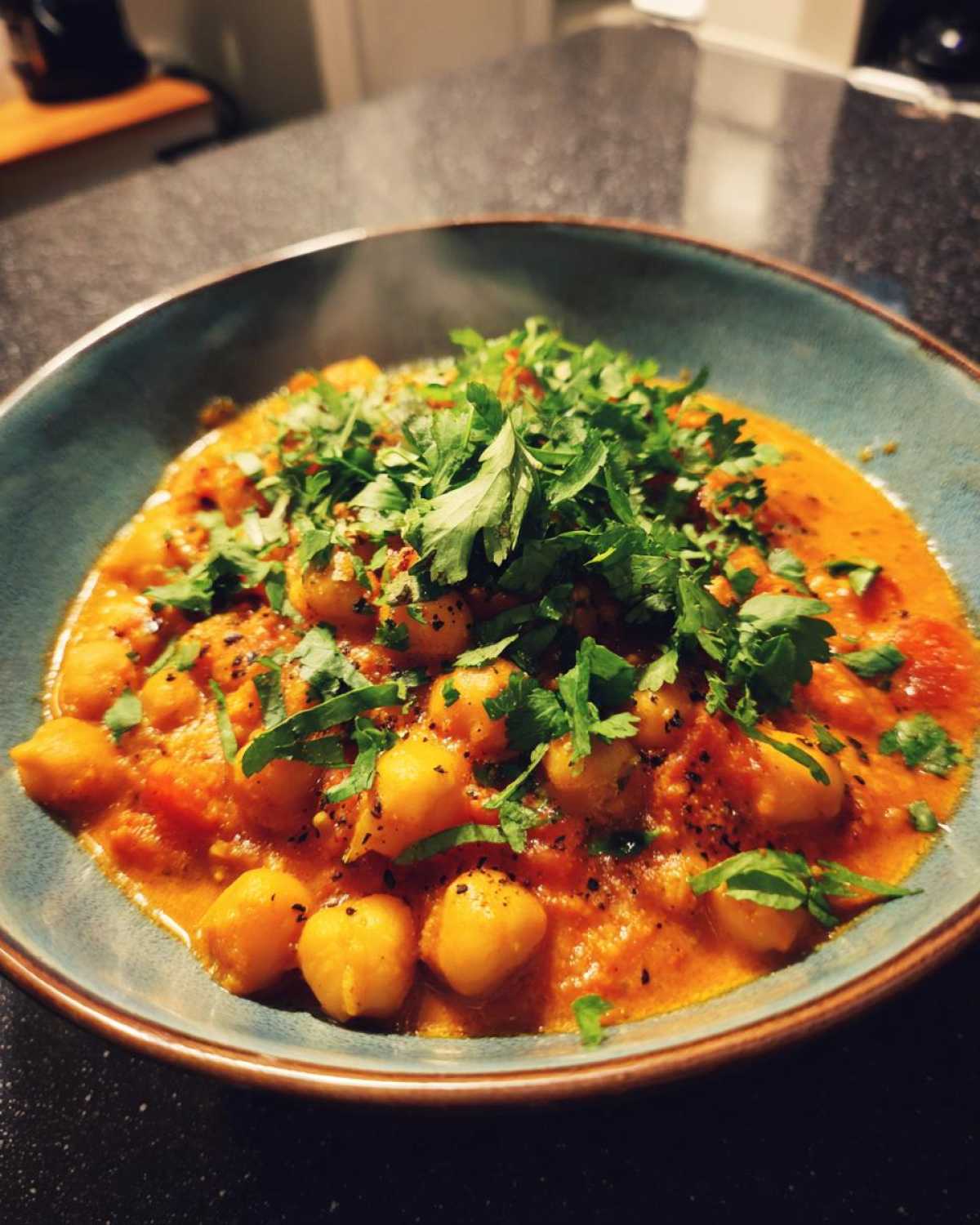 Aromatyczne curry z ciecierzycą podane w niebieskiej misce, posypane świeżą kolendrą.