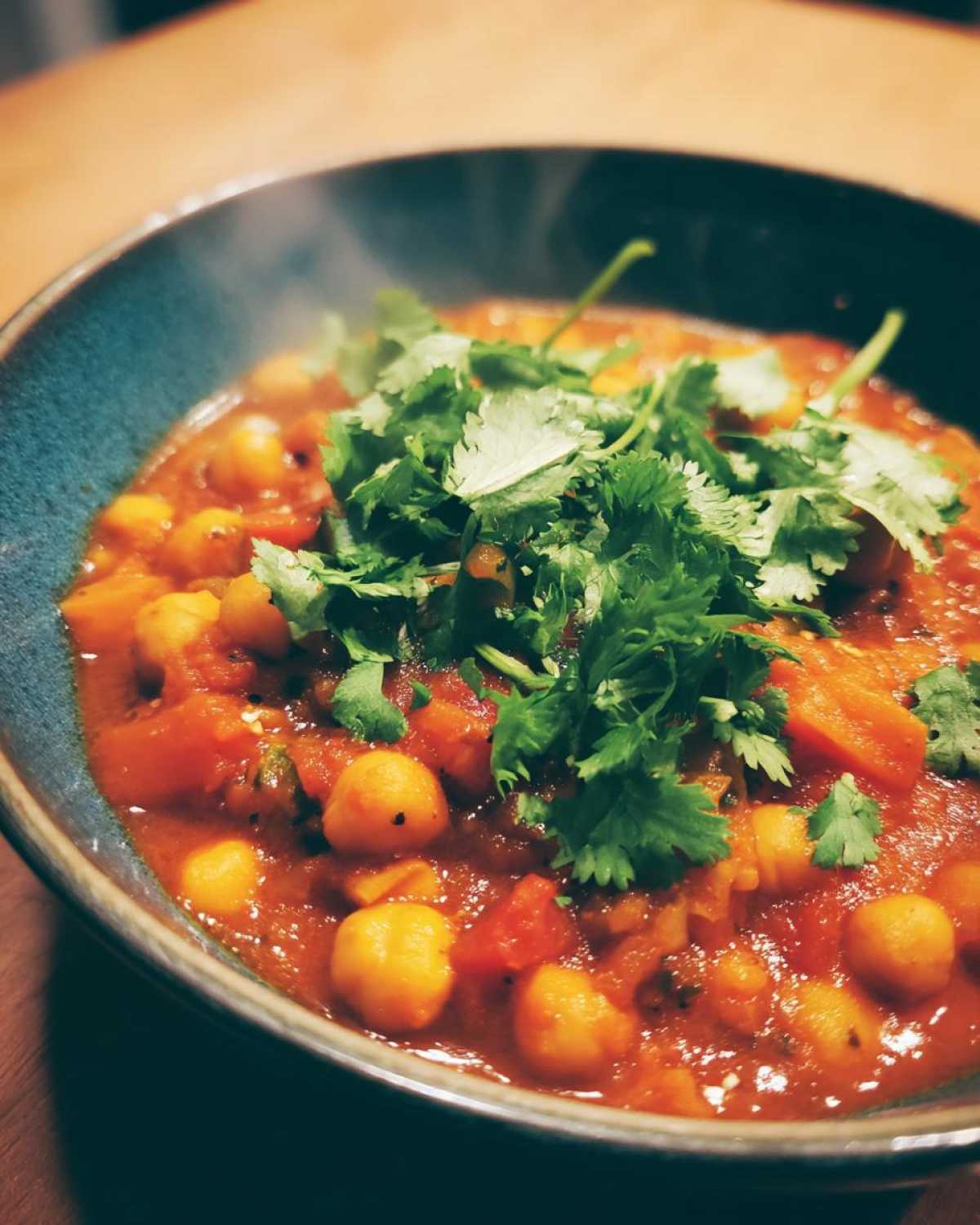 Aromatyczne curry z ciecierzycą w niebieskiej misce, udekorowane świeżą kolendrą.