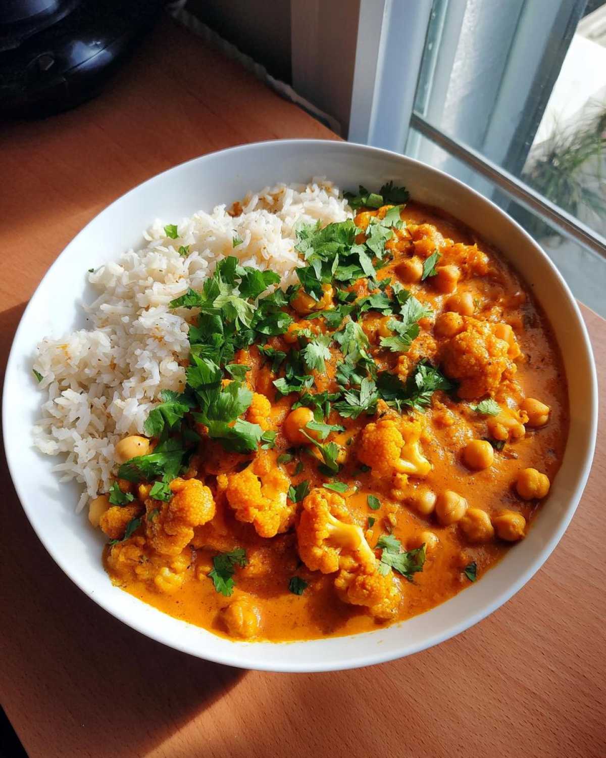Miseczka pełna curry z kalafiorem, ciecierzycą i ryżem, posypana świeżą kolendrą.