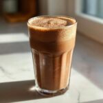 Szklanka z orzeźwiającym czekoladowym shake'iem białkowym, z pianką na wierzchu.