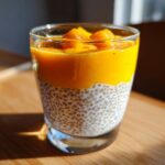 Deser chia z mango w szklance, warstwowy, z kawałkami mango na wierzchu.