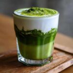 Szklanka domowej matcha latte z gęstą pianką i posypką z zielonej herbaty matcha.