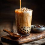 Zbliżenie na szklankę domowego bubble tea, do której nalewane jest mleko, z widocznymi kuleczkami tapioki i lodem.