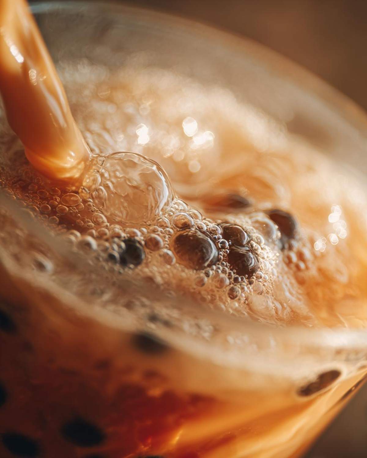 Zbliżenie na nalewany do szklanki napój do domowego bubble tea, z widocznymi bąbelkami i tapioką.